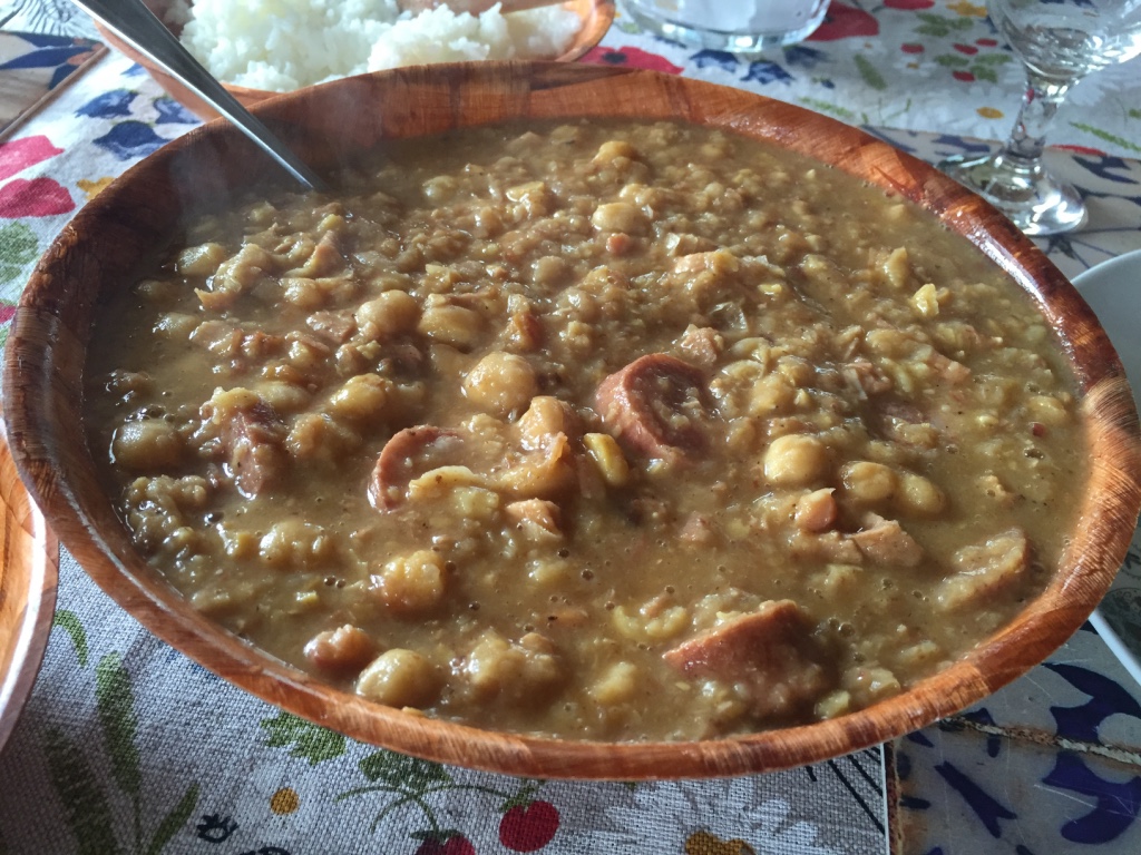 INGREDIENTES E MODO DE PREPARO Cozinhe o grão de bico na água e sal, escorra e reserve; Frite o banco em cubinhos até dourar; Adicione cebola picada e alho socado e frite até dourar a cebola; Adicione a lingüiça calabresa em rodelas, frite; Adicione o grão de bico, refogue e adicione água; Tampe a panela e deixe cozinhar até formar um caldo grosso (mexa sempre para não queimar no fundo da panela); Ajuste o sal. DICAS - Pode usar outras carnes secas; - Na receita acima usamos as sobras do pernil do réveillon.